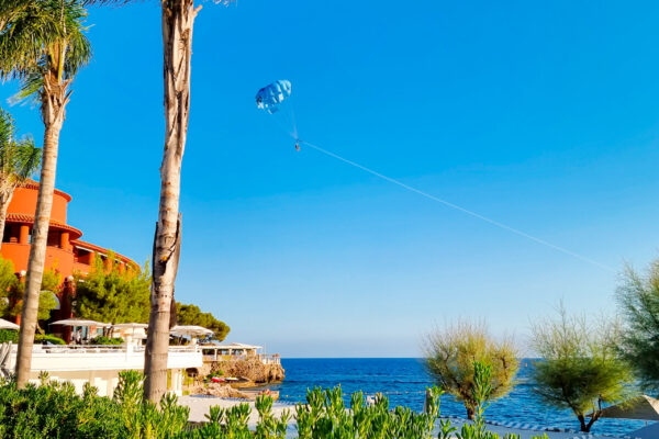 parasailing-monaco-hotel-balneaire-plage Vol en parasailing vu depuis la plage d'un hôtel balnéaire près de Monaco, palmiers et Méditerranée