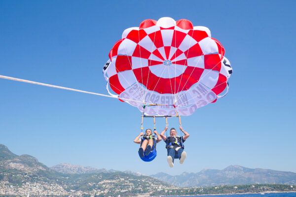 vol-duo-parachute-ascensionnel-monaco-cote-azur Deux passagers en vol duo en parachute ascensionnel au-dessus de Monaco, côte entre Roquebrune et Menton en fond
